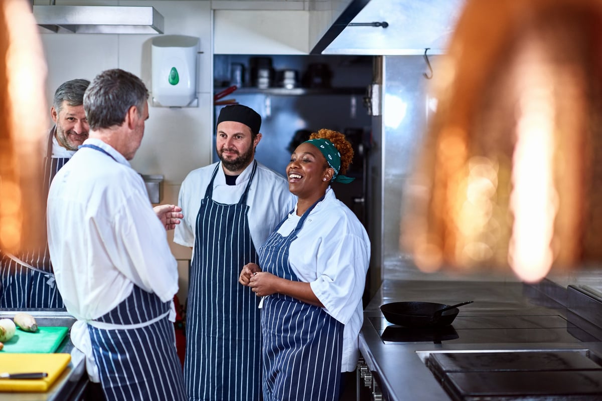Four chefs stand in a restaurant kitchen and chat.