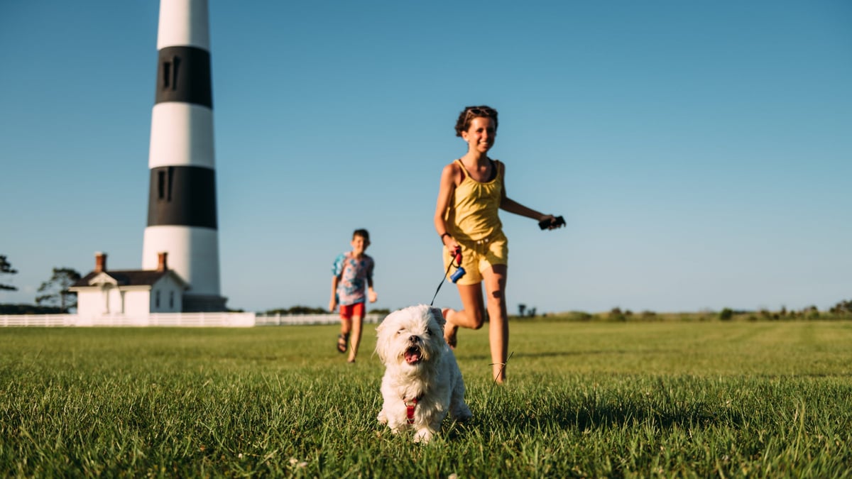 Children walking dog near a lighthouse.
