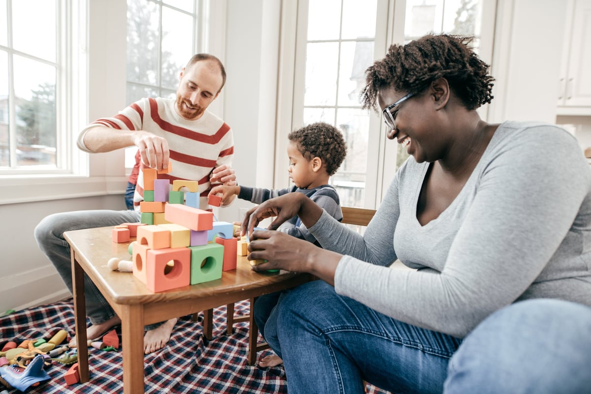 A couple and their son play with building blocks at home.