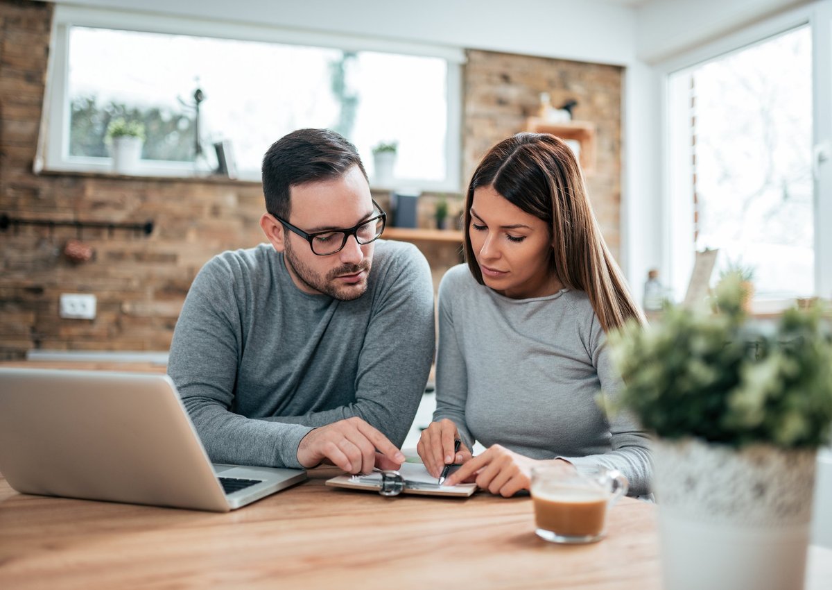 A couple paying their bills at a table with a laptop and notebook.