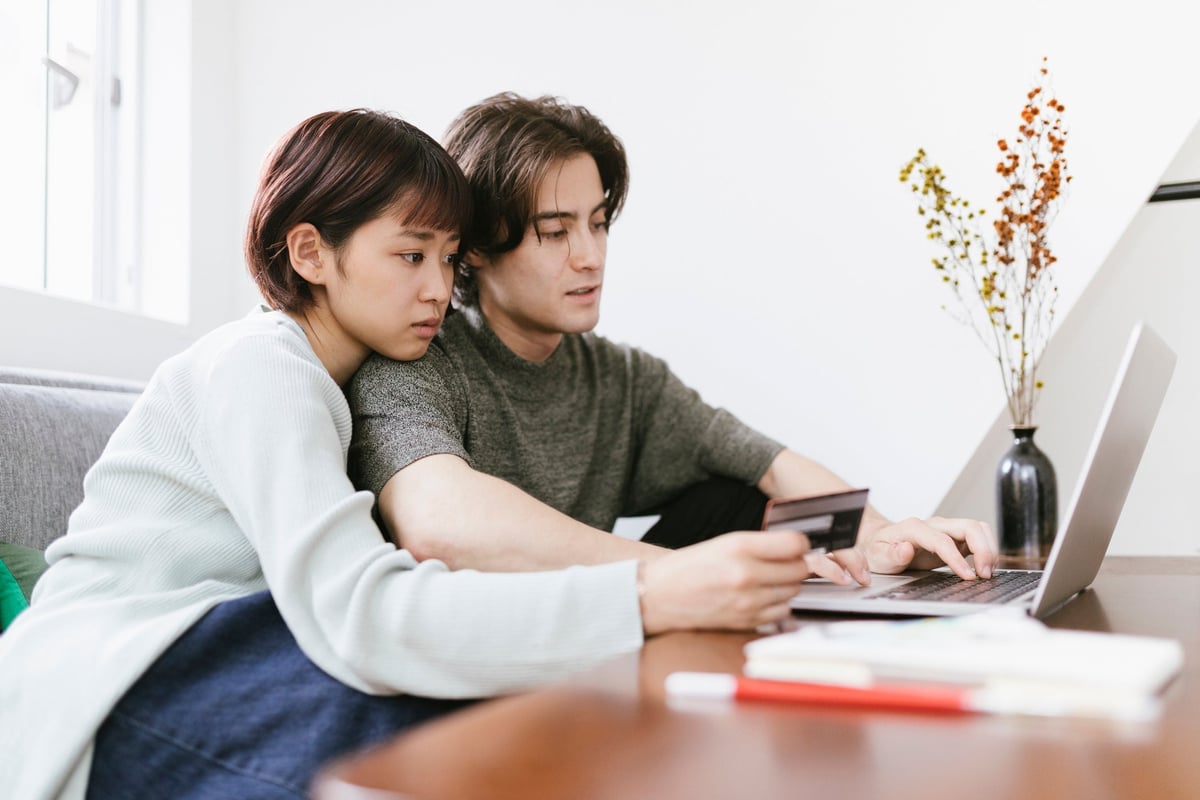 A couple sit together on the couch, preparing to make an online purchase.