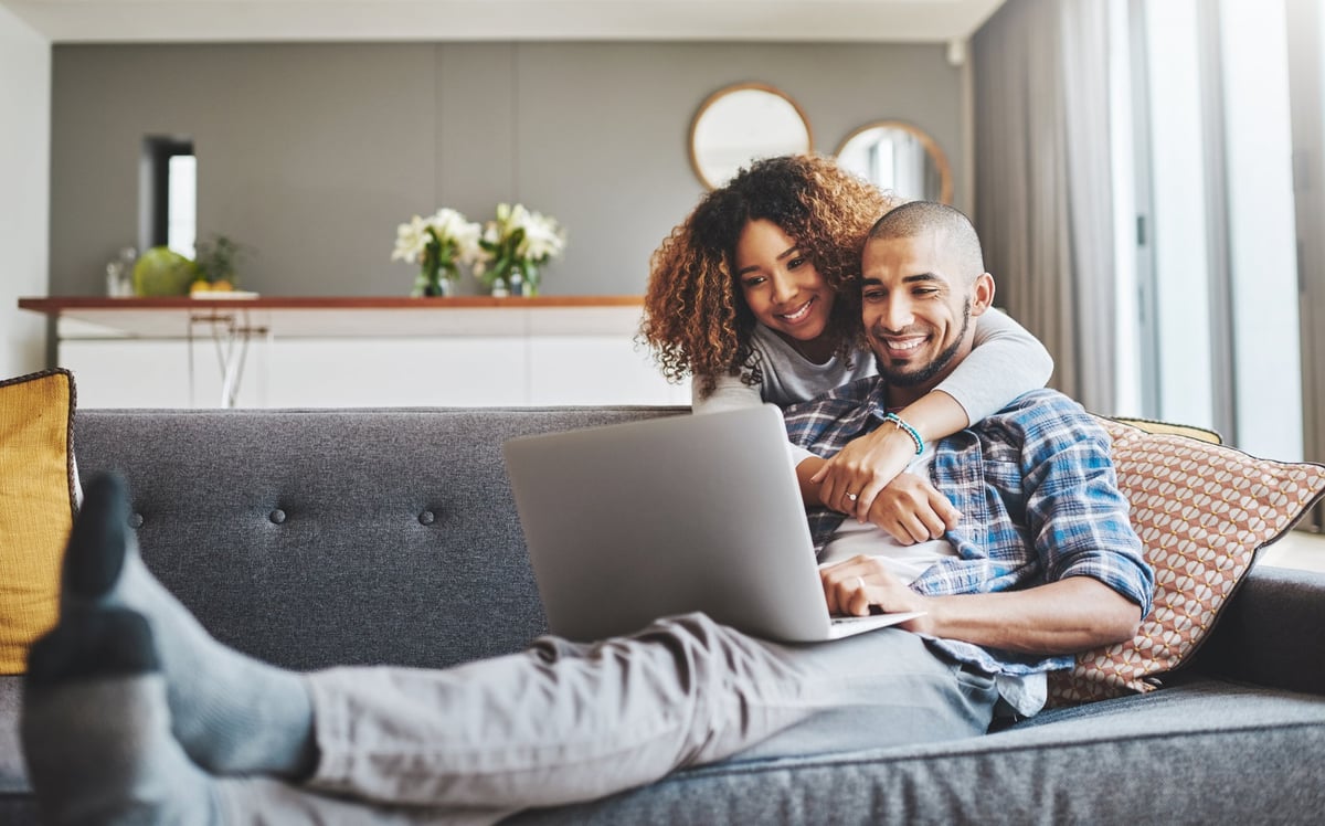 A couple smile and look at a laptop together.