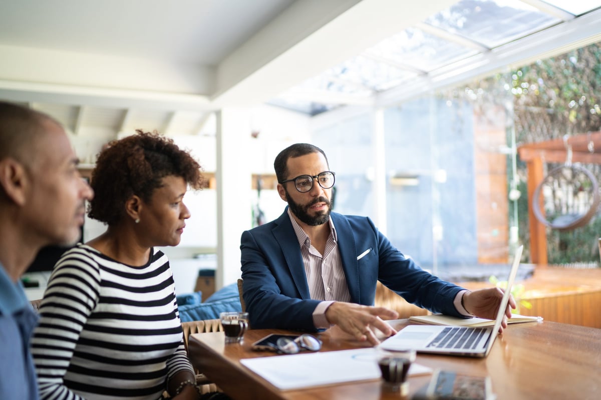 Couple speaking with professional male who shows them something on a laptop.