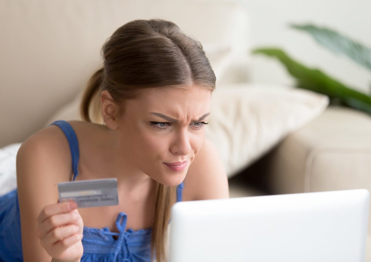 A woman looking confused at her computer while holding a credit card.