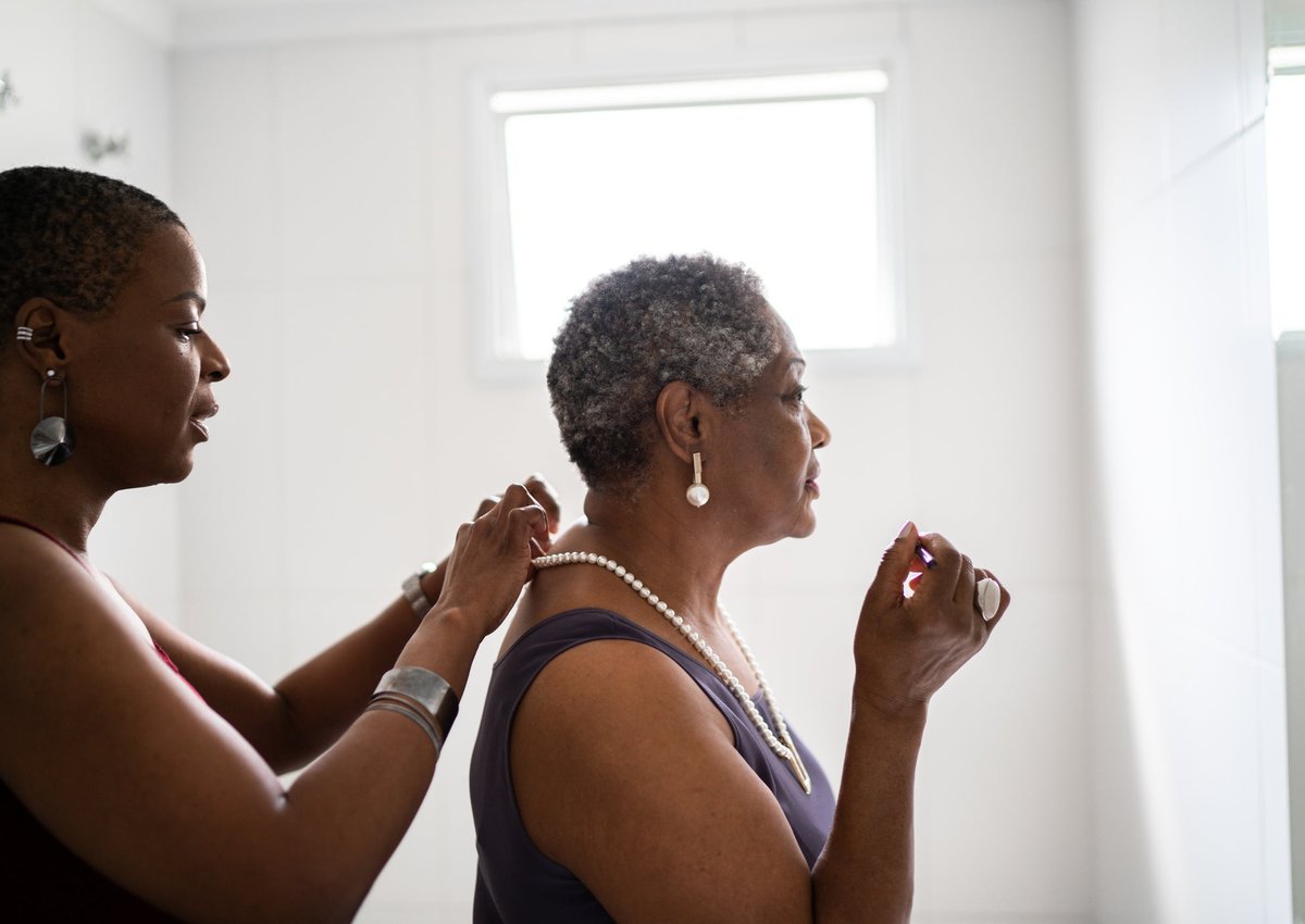 A daughter fastens a pearl necklace for her mother.