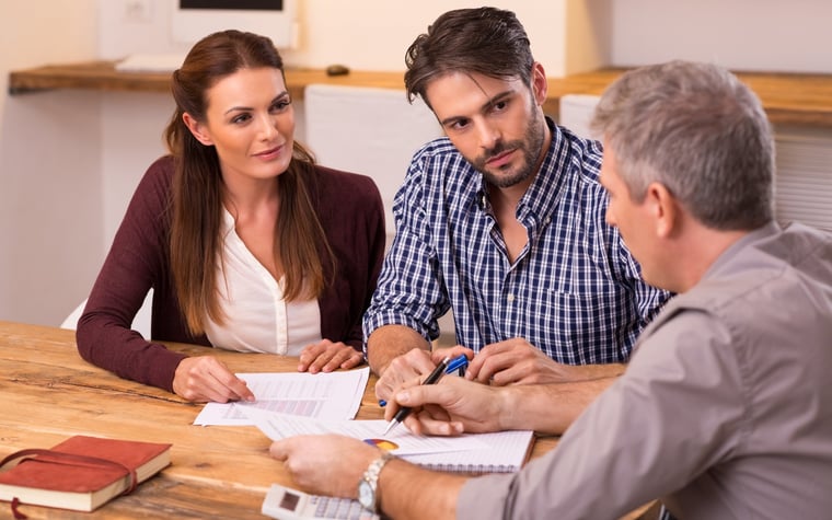 Three people sitting around a table with a calculator going over paperwork.