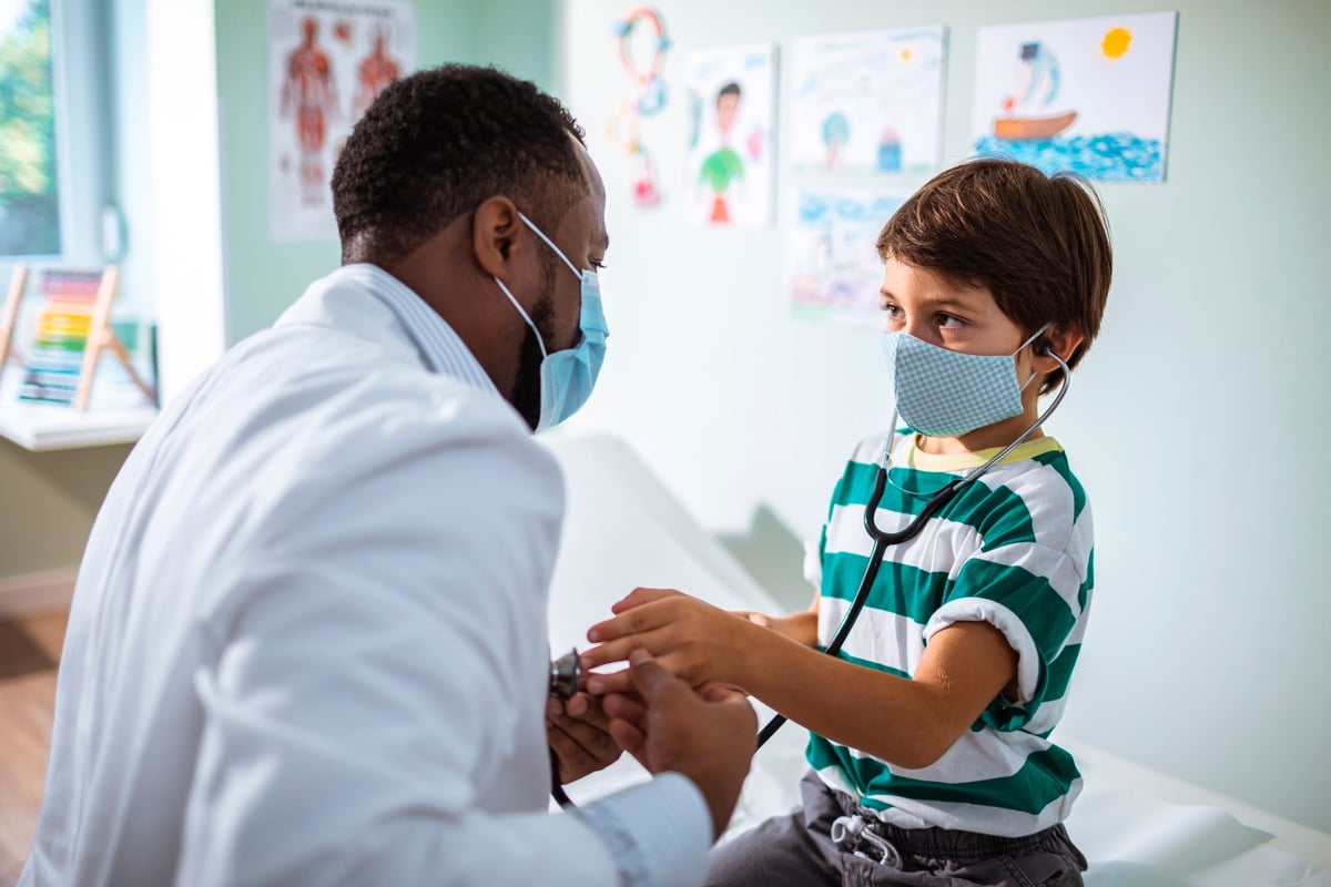 A doctor lets a young boy use his stethoscope.