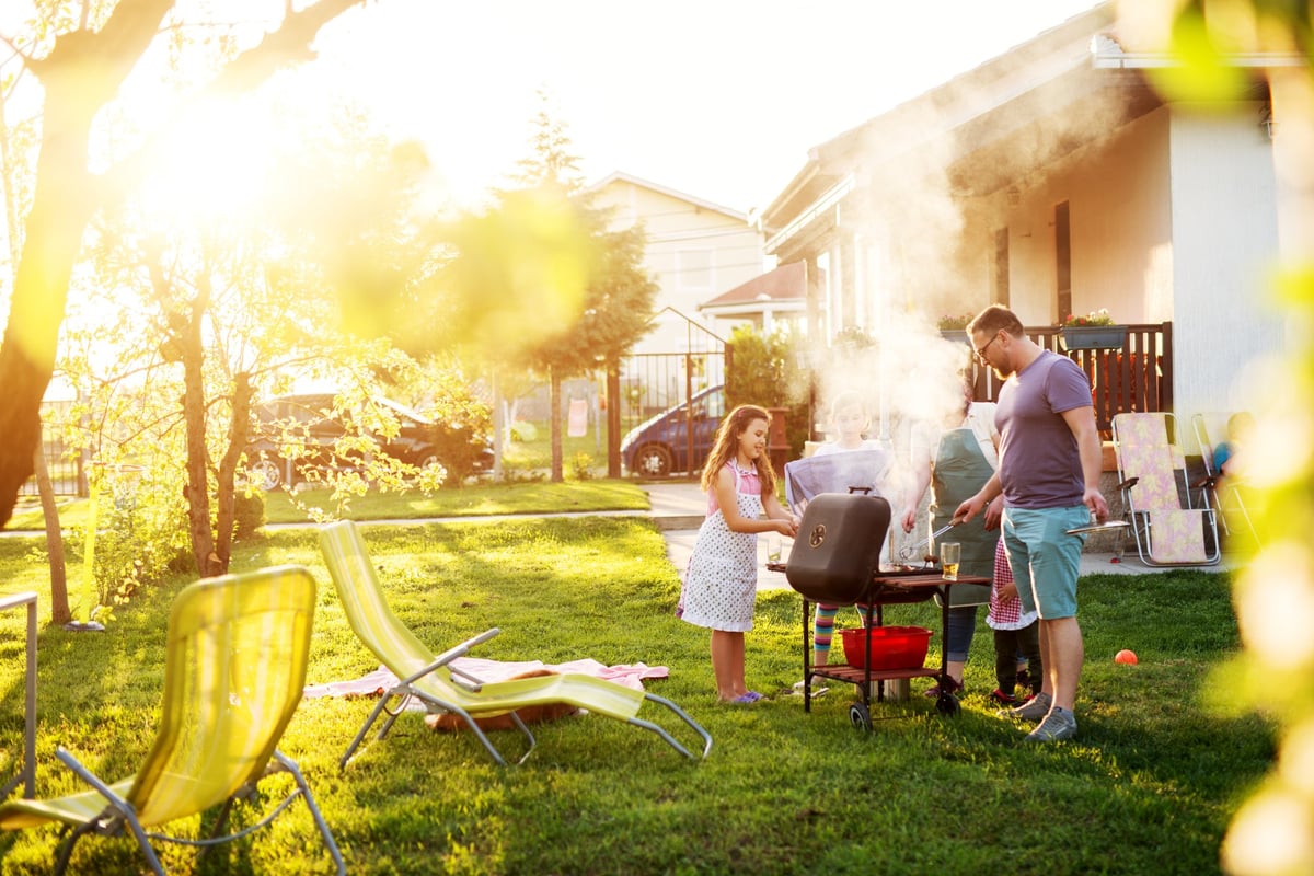 A family barbecuing in a sunny backyard.