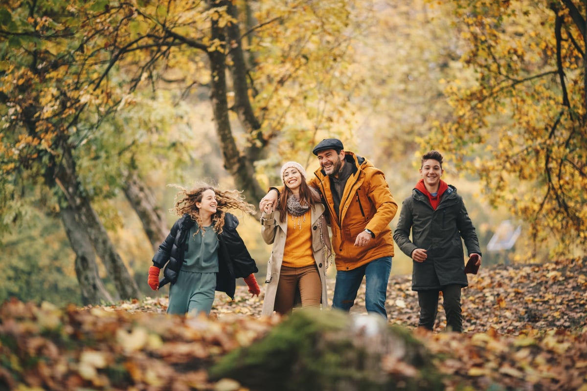 A family walks through a forest, enjoying the fall foliage.