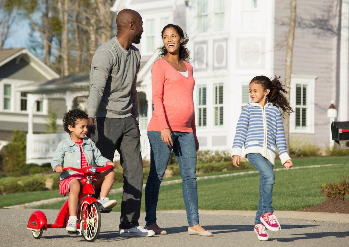 Couple walking through suburban neighborhood with youngest child riding a tricycle.