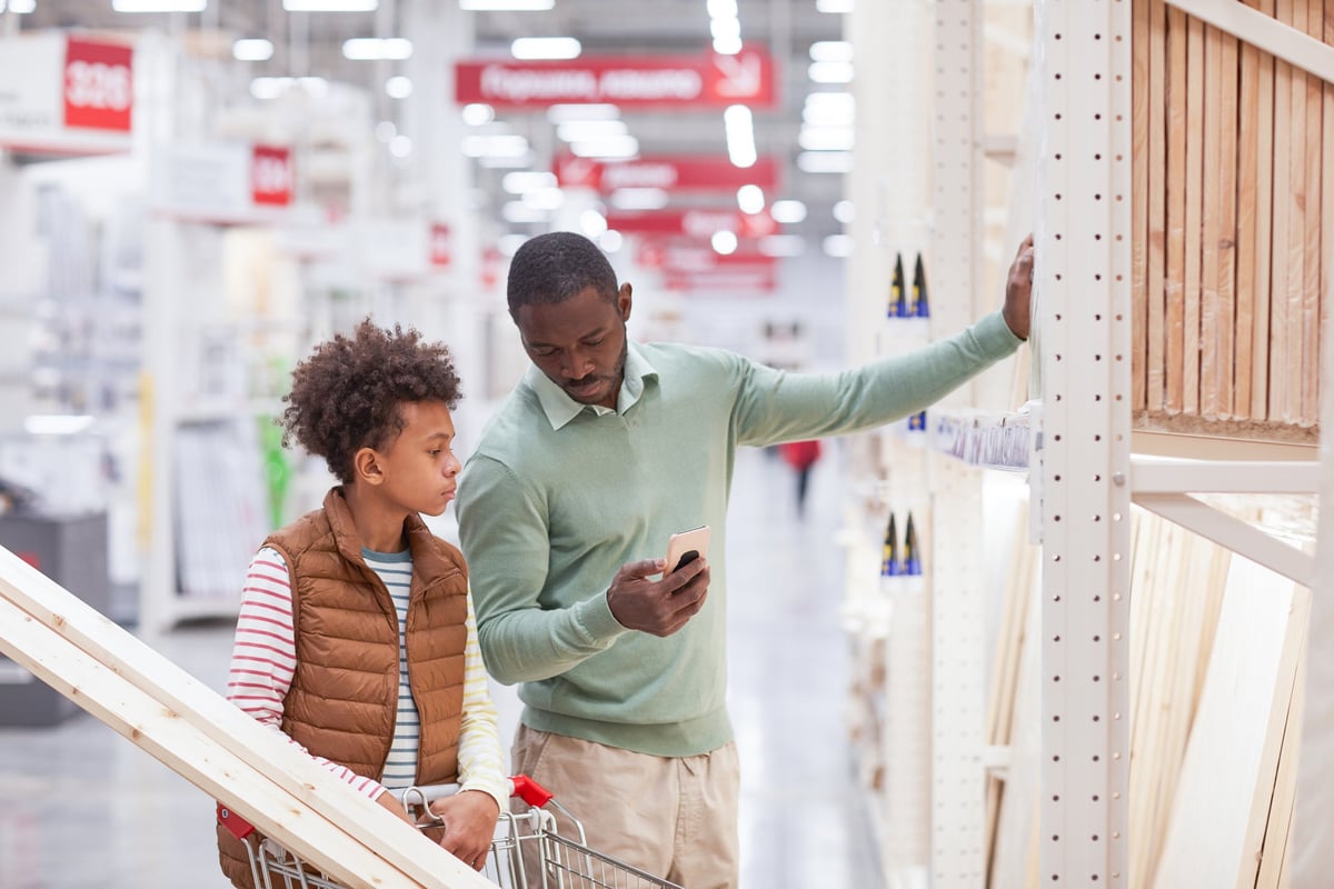 A father and son stand inside a home improvement store, looking at lumber.