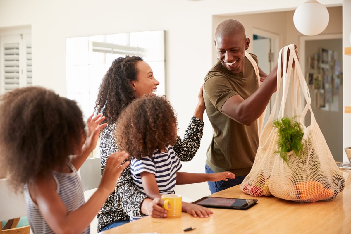 A smiling father bringing home groceries to his family.