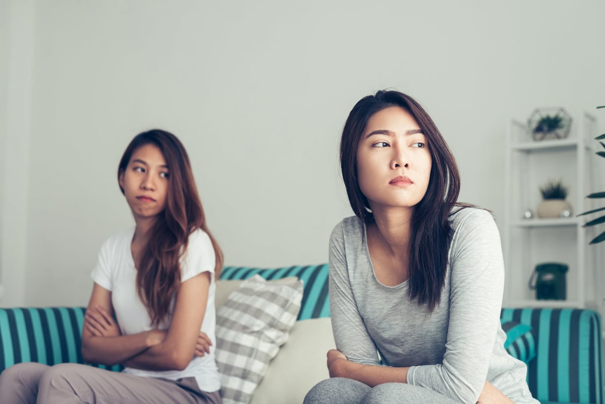 Two women sitting on a couch, one with her arms crossed and the other looking away.