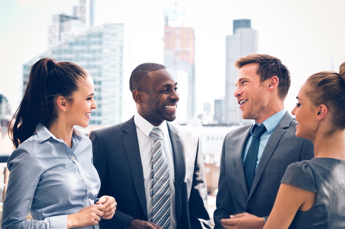 Four friends in business attire stand outside and laugh.