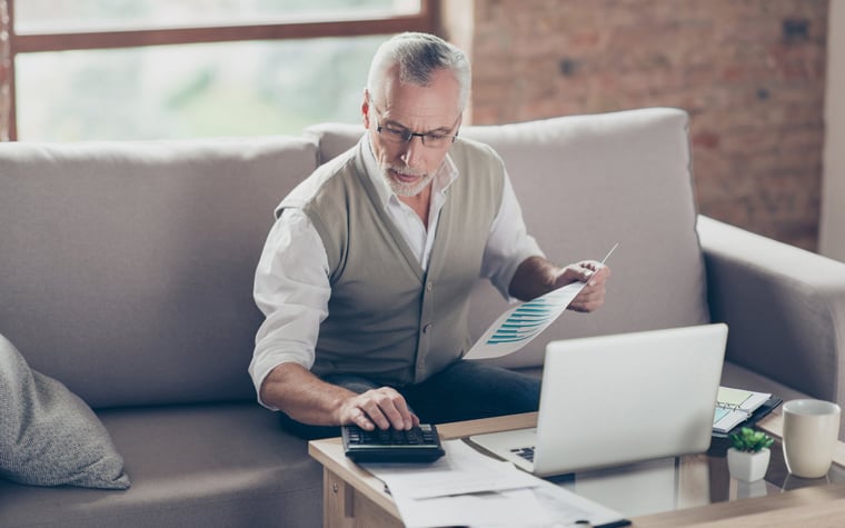 Older man using calculator and laptop.