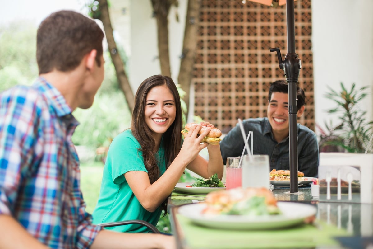 Friends sitting outdoors eating sub sandwiches.