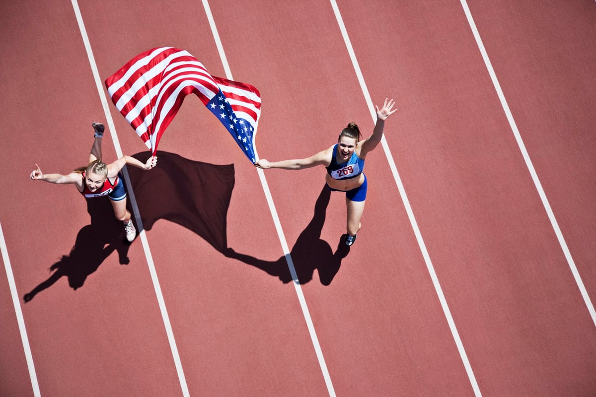Bird's eye view of two female track runners holding an American flag and waving.