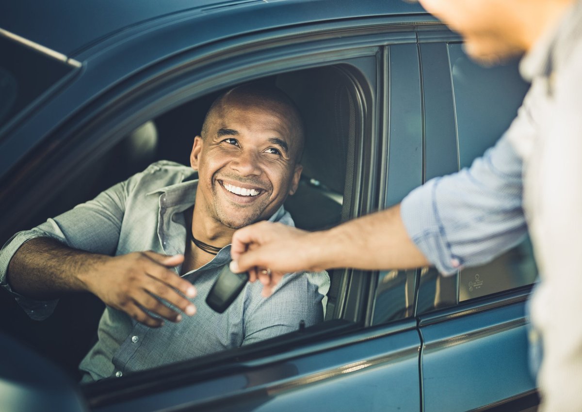 A smiling person in a car receives car keys.