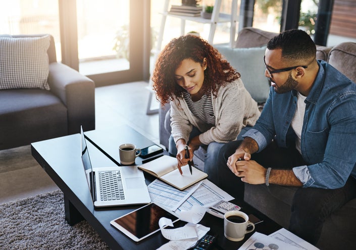 Couple discusses finances in living room with laptop and charts.