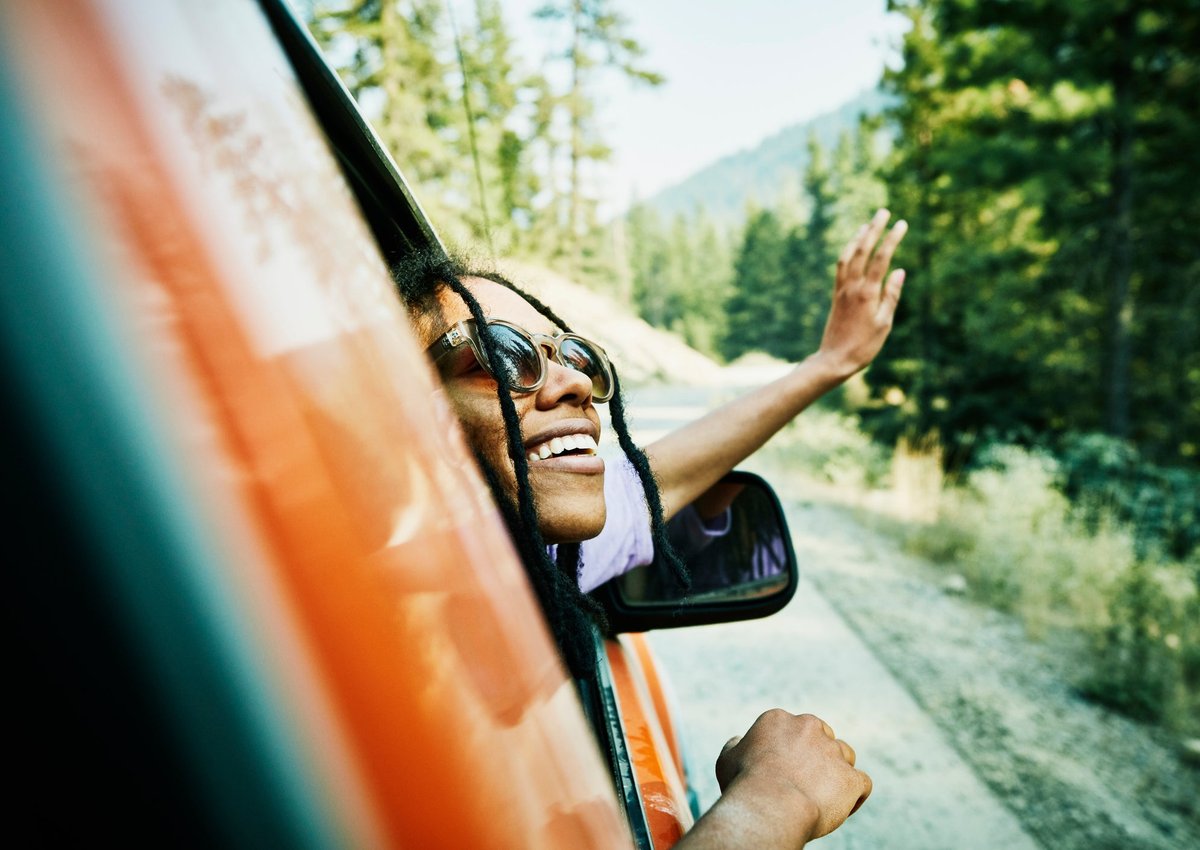 A person leans out the passenger side's window of a red car, smiling.