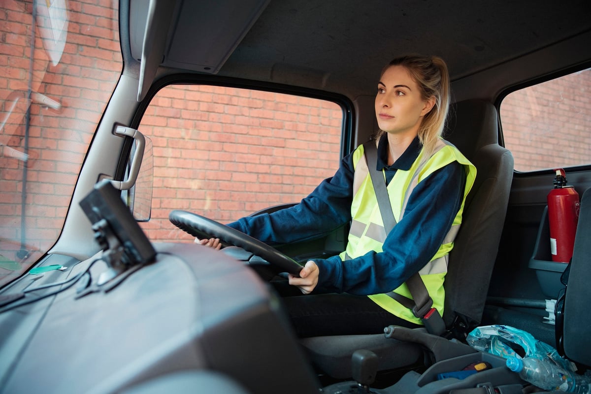 A young adult manual worker drives to work in a van wearing their uniform.