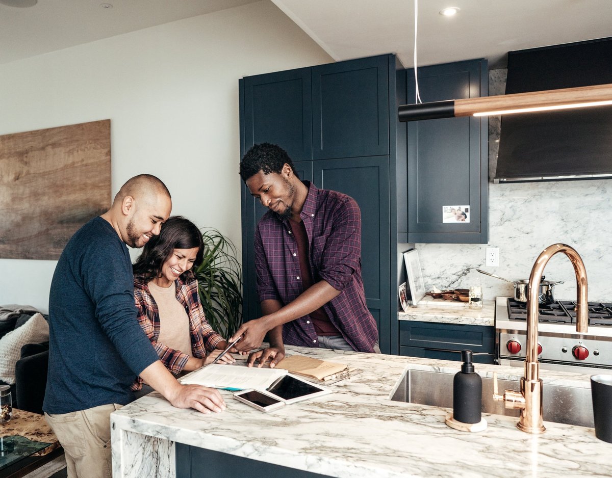 A family meets with a realtor, who points at paperwork and smiles in a kitchen.
