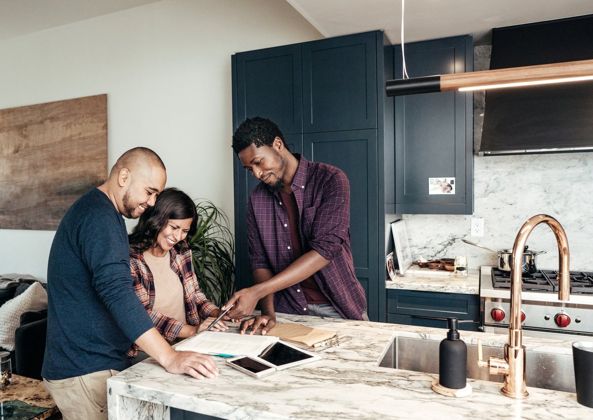 A family meets with a realtor, who points at paperwork and smiles in a kitchen.