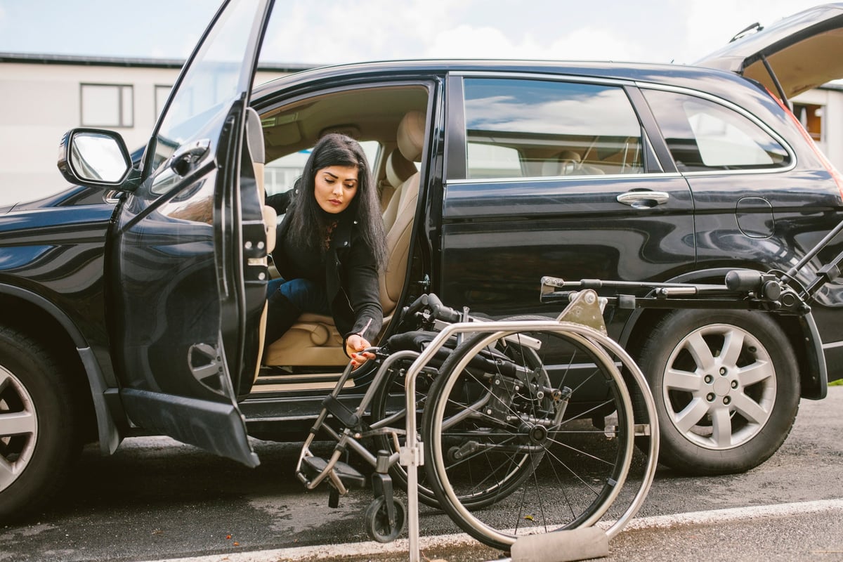Someone pulls their wheelchair into their vehicle while parked in a parking spot.