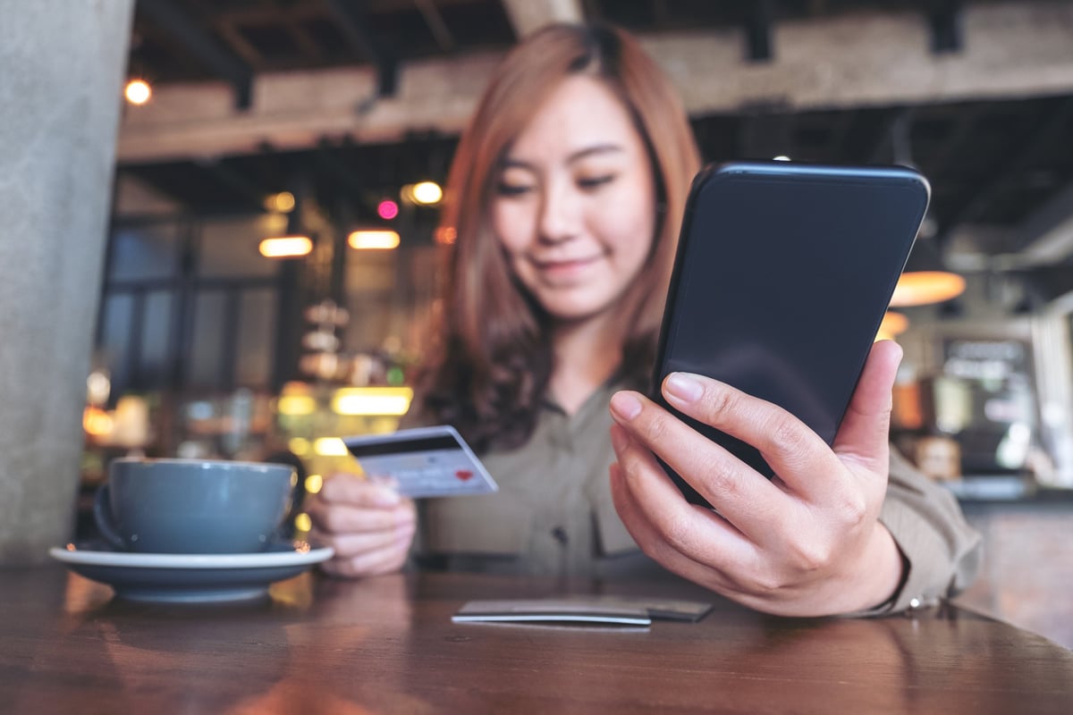 Young woman in coffee shop smiling at her credit card and phone.