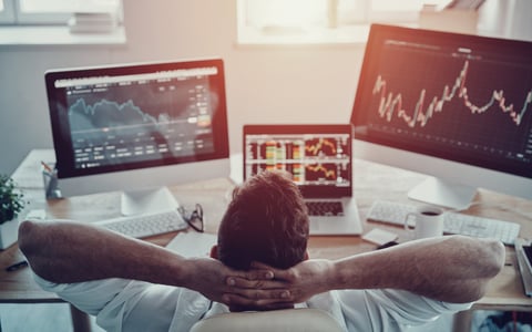 Guy leaning back and monitoring three screens featuring various stock information.