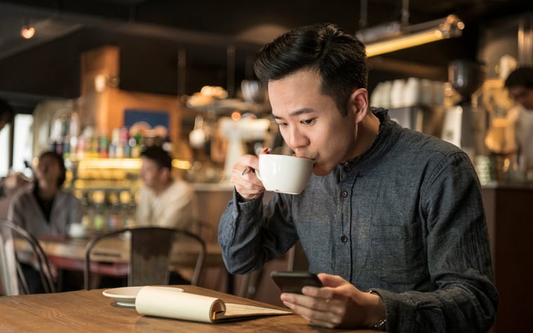 A young businessperson does paperwork in coffee shop and checks their phone.