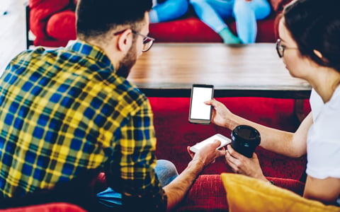 Two people show each other their phones while drinking coffee.