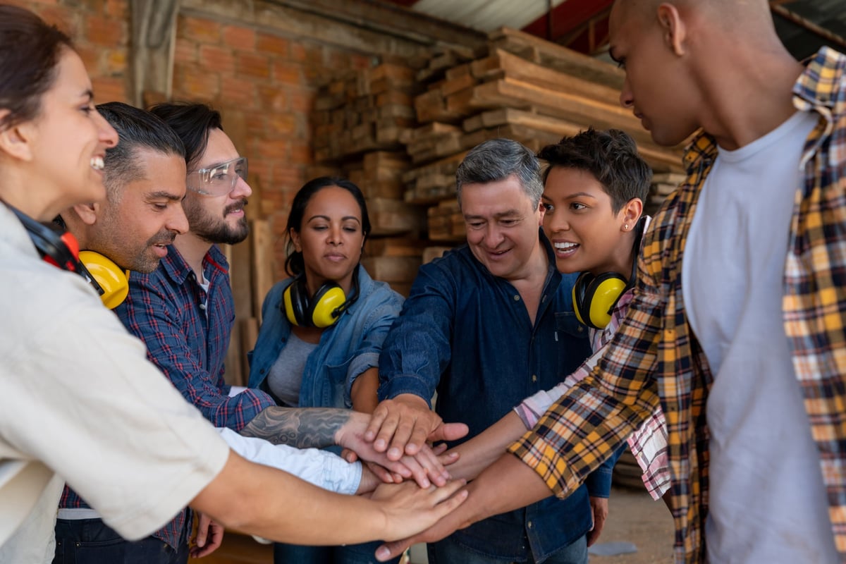 Some workers at a wood factory put their hands together while smiling.