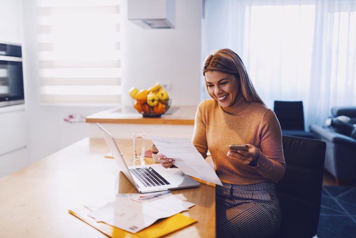 Happy woman reviewing documents and laptop at home