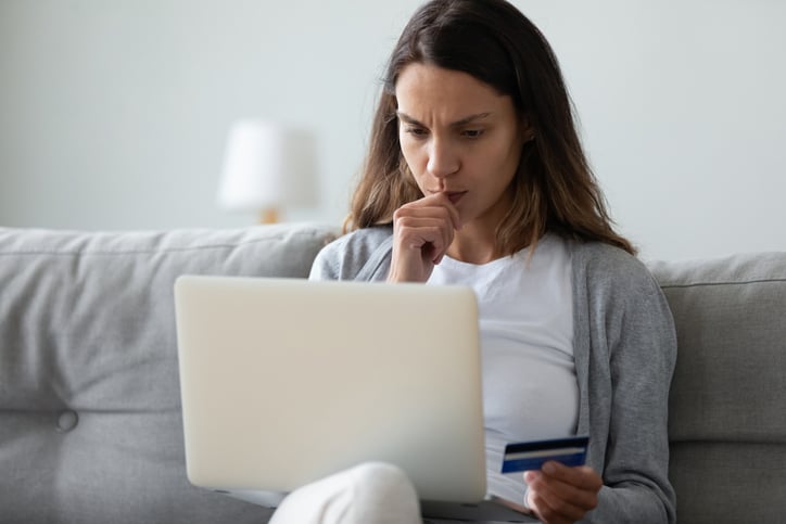Woman on sofa with credit card in her hand and laptop.