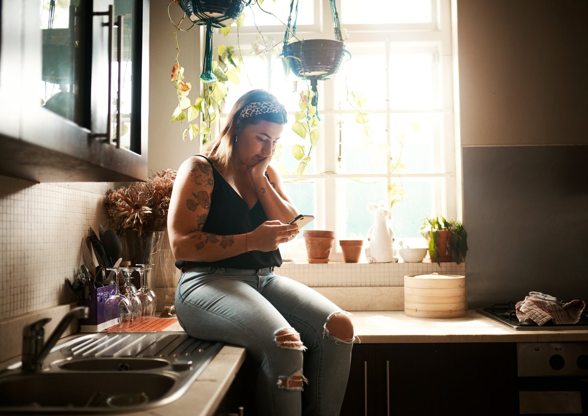 Woman sits on counter in a kitchen, looking at her phone