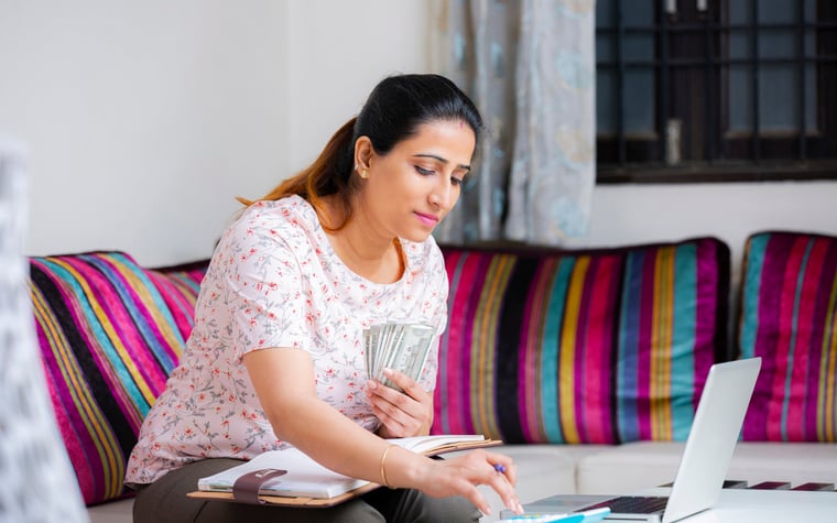 Woman sitting on a sofa with cash and using a calculator.