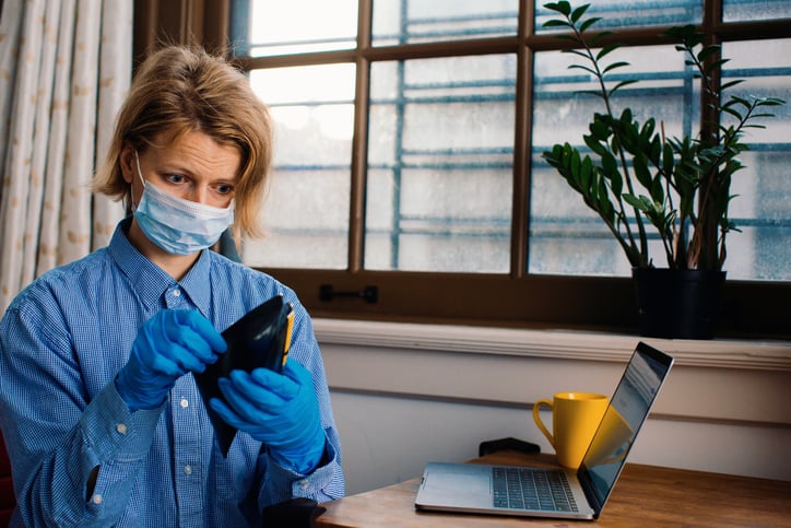 Woman in mask and gloves looks into empty wallet.