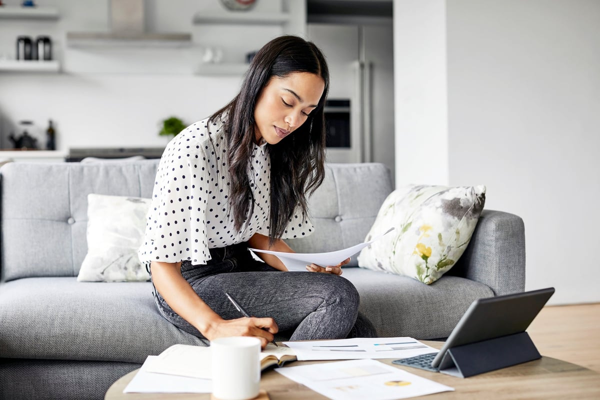 A young woman reviews her personal finances using print-outs and a tablet at home.