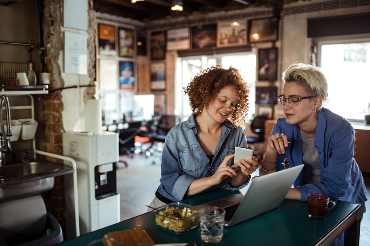 Two people use a smartphone in a casual office setting.