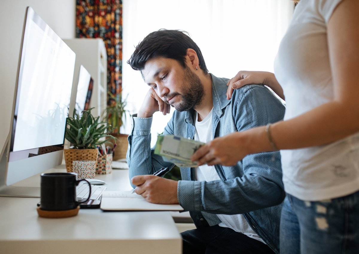 Someone frowns at their notebook as their partner hands them a bill.