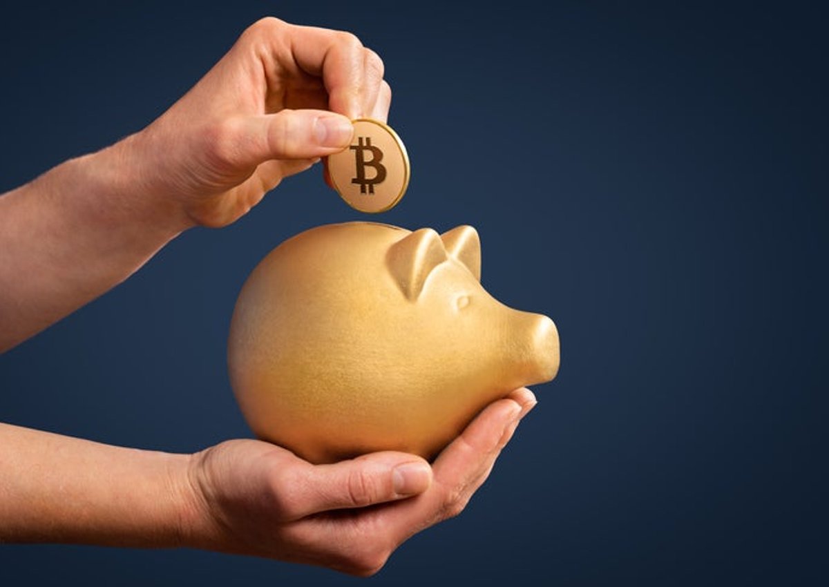 Person inserts Bitcoin into a gold piggy bank.
