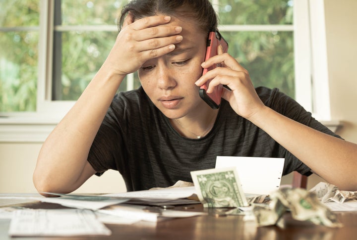 Stressed woman holding phone looks at bills.