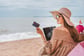 Woman wearing sun hat sits on a beach holding a credit card. image for Best Travel Credit Cards