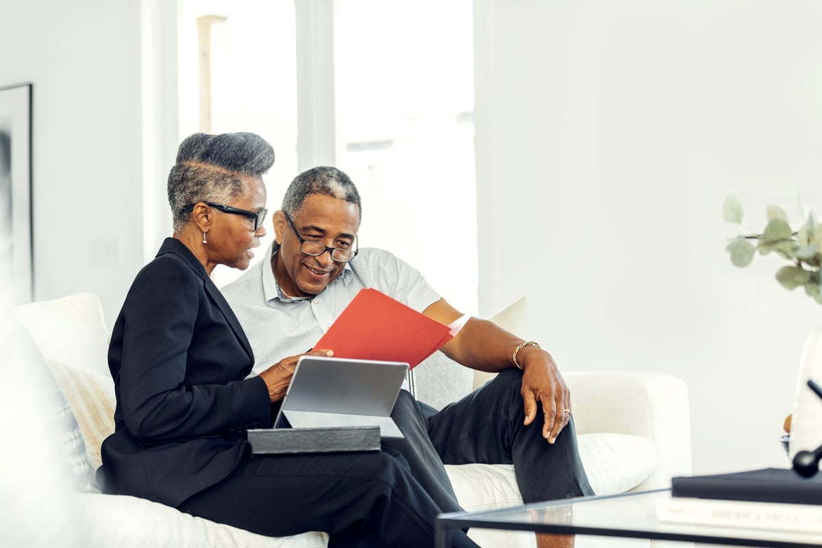 Deux adultes plus âgés discutent de finances à l'aide d'une tablette sur un canapé.