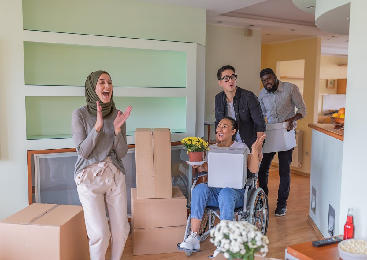 Four adults, including one using a wheelchair, gasp in delight at their new home surrounded by moving boxes.
