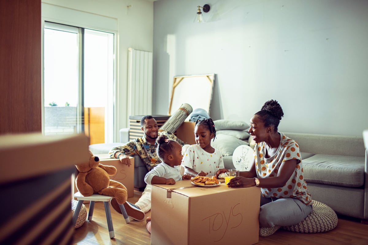 A family eats breakfast on top of cardboard moving boxes in their new home.