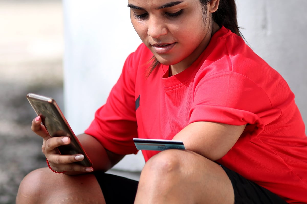 A person with an amputated left limb uses a credit card and smartphone to shop online while outside.