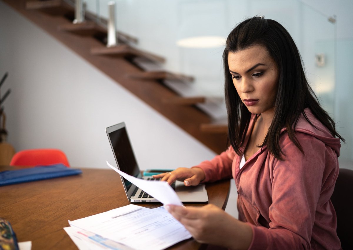 An adult sits at home at a desk and reviews financial documents.
