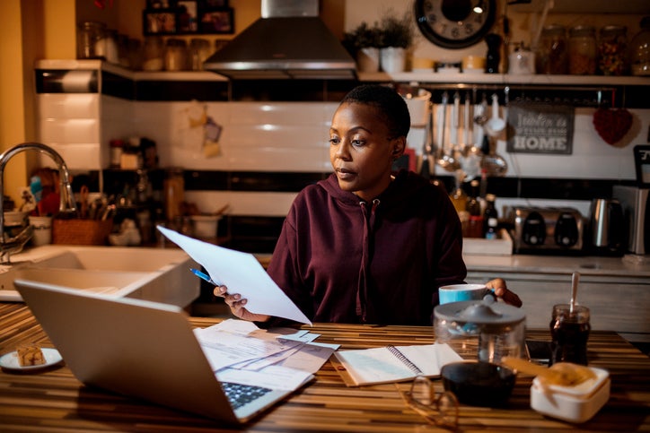 Young adult does their home finances at a laptop in the kitchen.